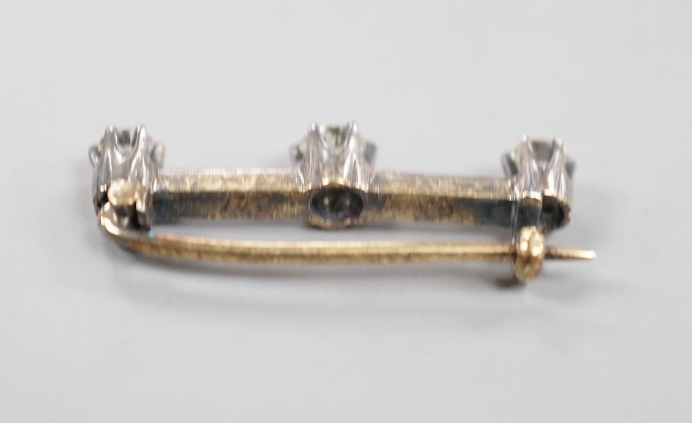 An early 20th century yellow metal and three stone diamond set bar brooch, 26mm, gross 2.1 grams.